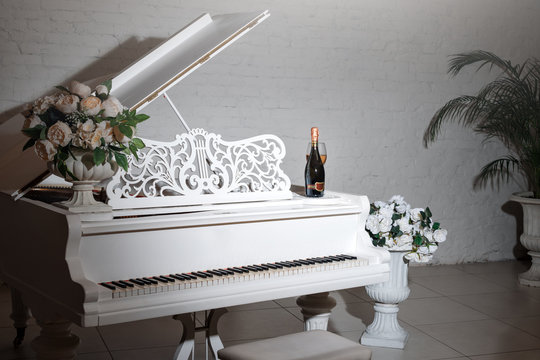 Grand piano in a luxury white classic interior with wine, palms and flowers.
