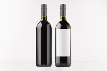 Two dark wine bottles with blank white label and without label, on white wooden board, mock up. Template for advertising, design, branding identity.