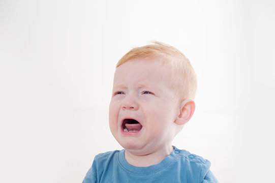 Redhead boy crying against white background