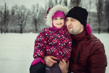 happy young father in claret coat with little daughter in pink pattern coat smiling, hugging and...