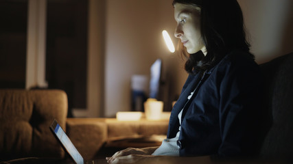 Young concentrated woman working at night using laptop computer and typing message