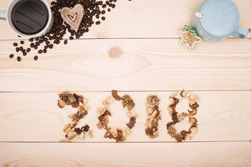2018 inscription of dried flowers,a cup of hot fragrant espresso, gingerbreads and a closed sugar bowl and scattered coffee beans on a light wooden background. Top view. Copyspace.