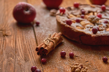 Sticks of cinnamon on wooden brown background. Powdered apple pie with fresh cranberries and...