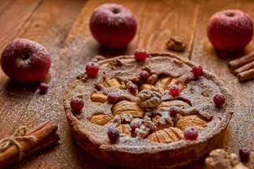 Powdered apple pie with fresh cranberries and walnuts decorated with apples and cinnamon. Powdered...