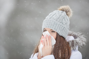 Girl with allergy symptom blowing nose. Teen girl using a tissue in a winter park