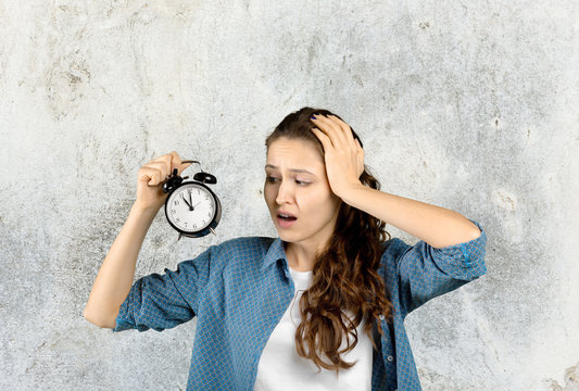 Surprised attractive young woman holding alarm clok