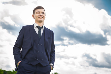 Strong asian groom in a dark blue smiling against the backdrop of beautiful sky. concept of a strong successful man