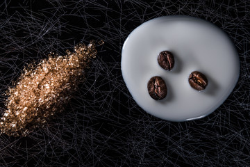 Coffee beans in spilled milk and brown sugar on a black and silver kitchen table top in hard, low key light - 183452490