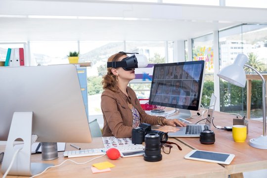 Female executive working on laptop while using virtual reality