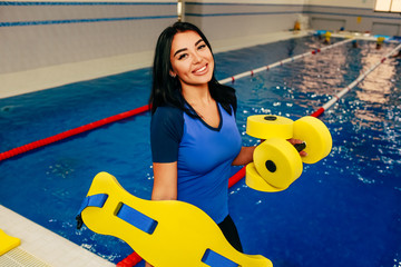 Sporty woman holding Fitness Barbells at swimming pool and positive looking at camera. Aqua Fitness instructor