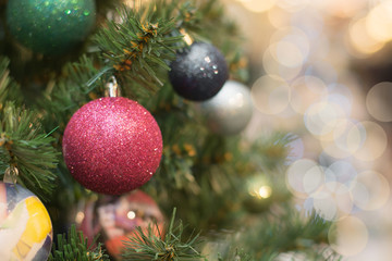 Christmas tree with holiday red balls and lights with copy space on blurred bokeh background in mall. Close up.