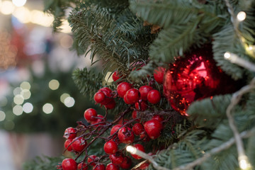 Christmas tree with holly berries as decor and lights with copy space on blurred bokeh background in mall. Close up.
