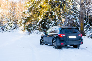 Fototapeta na wymiar Winter tires. Black Subaru Outback rear view on snowy forest road. Winter conditions.