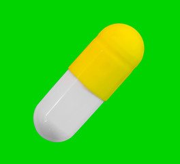 a gelatin capsule with yellow cap isolated on green background closeup, top view