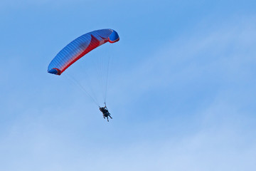 Vol en parapente avec aile bleue et rouge sur fond de ciel bleu d'été dans un brume de chaleur.
