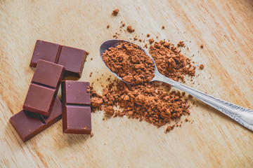 Dark chocolate with cocoa powder on wooden table