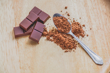 Dark chocolate with cocoa powder on wooden table