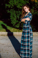 Fashion outdoor photo of beautiful young woman in elegant blue dress. Portrait of gorgeous long hair woman in checkered dress posing outdoors.