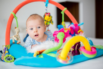 Cute baby boy on colorful gym, playing with hanging toys at home © Tomsickova