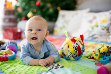 Happy three months old baby boy, playing at home on a colorful activity blanket - obrazy, fototapety, plakaty