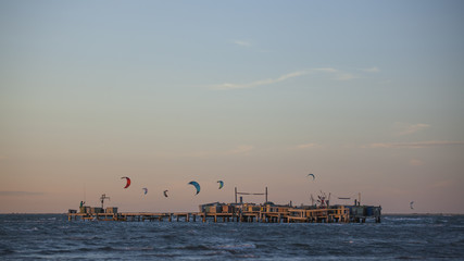 Kitesurf, parapente et voile delta au-dessus de la mer Méditerranée sur une plage de Camargue au soleil couchant.