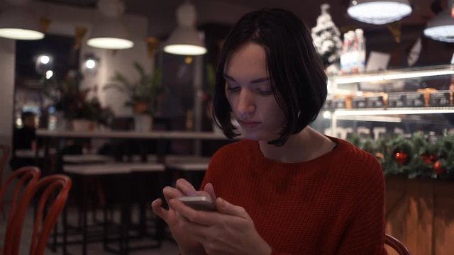 Cute young woman texting message using smartphone sitting in cafe.