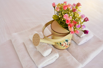 Freshly laundered fluffy white towels on bed in hotel or Beautiful lilly on towels rolls and colorful flower Jar - Holiday of concpet