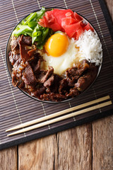 Gyudon beef with rice, egg and onion closeup in a bowl on the table. Vertical top view