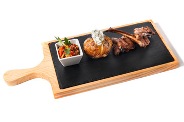 Deep grilled barbecue rib on wooden cutting plate with garnish - uncleaned boiled potato with parmesan cheese and vegetable salad with parsley leaf. Isolated on white