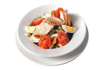 Caesar salad with chicken, eggs, cherry tomatoes and parmesan on round plate. Isolated on white