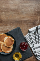 top view of tasty pancakes with maple syrup and jam on wooden table