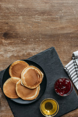 top view of delicious pancakes with maple syrup and jam on wooden table