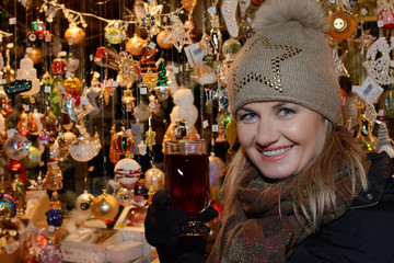 Young woman standing at the street and drinking hot punch in the Christmas market.