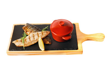 Grilled salmon fillet with garnish - lemon and arugula on wooden cutting plate with ceramic base. Red cloused pan. Isolated on white