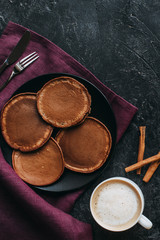 top view of chocolate pancakes and cup of coffee on black concrete surface