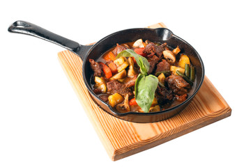 Cooking Stew meat in cast iron frying pan with carrots, onion and green basil on wooden cutting plate. Cherry tomatoes, mushrooms champignons, asparagus, potatoes. Isolated on white