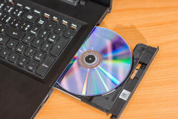 DVD ROM inserted in laptop computer on wooden texture background