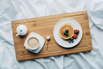 top view of breakfast in bed with tasty pancakes and coffee on wooden tray