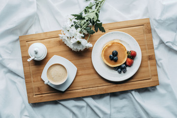 top view of breakfast in bed with delicious pancakes and coffee on wooden tray