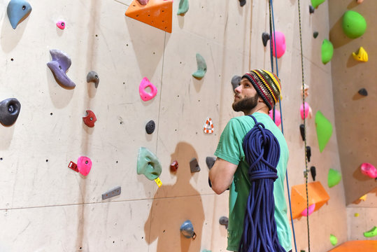 Kletterer vor einer Wand mit Kletterseil in einer Sporthalle // Climber in front of a wall with climbing rope in a sports hall