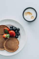 top view of chocolate pancakes with berries and cup of coffee on white table