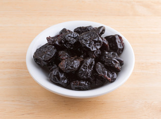 A portion of dried bing cherries in a small white bowl atop a wood table.