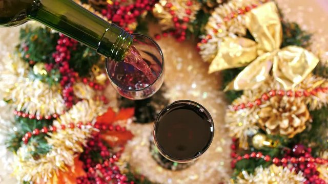 Red wine pouring into a glass .Glasses stand on the table with christmas wreath. Top view.