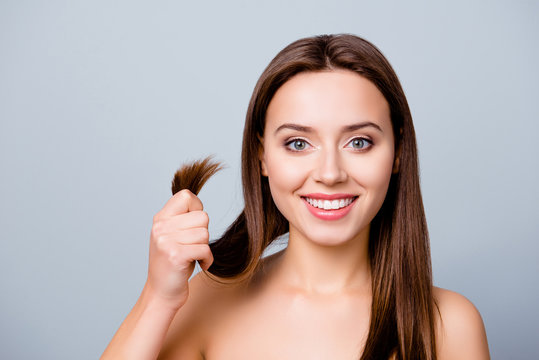 Concept Of Finding A Good Solution In Treating Damaged Hair Ends. Pretty Cute Smiling Woman Is Showing Her Healthy Hair, Isolated On Grey Background