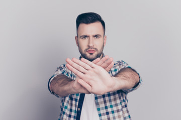 Prohibition symbol. Closeup portrait of young, serious man in checkered shirt making stop gesture with two crossed palms in front of himself on grey background