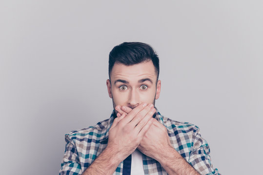 Oops! Close up portrait of attractive man closed his mouth with crossed hands and wide opened eyes, looking at camera, he can't believe his eyes, standing over grey background