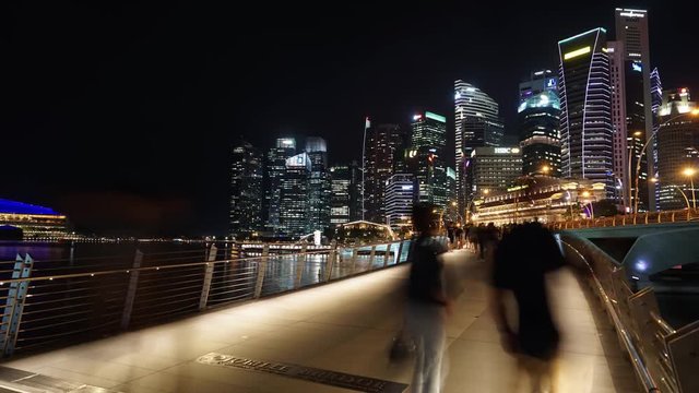 Singapore - November 27, 2017: Timelapse footage of Singapore downtown at night with skyscrapers view and pedestrian on the Esplanade Bridge. Shot in 4k resolution