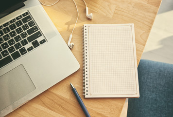 Notepad, laptop and headphones on the wooden desk