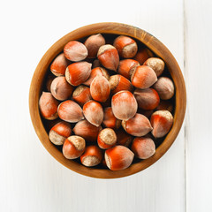 Hazelnut nuts in a wooden bowl on a white wooden table. Superfood.