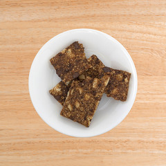 Top view of several broken almond butter chocolate nut bars on a plate atop a wood table.